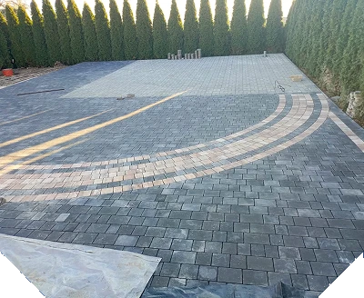 Układanie kostki brukowej podjazdu z szarej i beżowej kostki z dekoracyjnymi łukami otoczonego żywopłotem