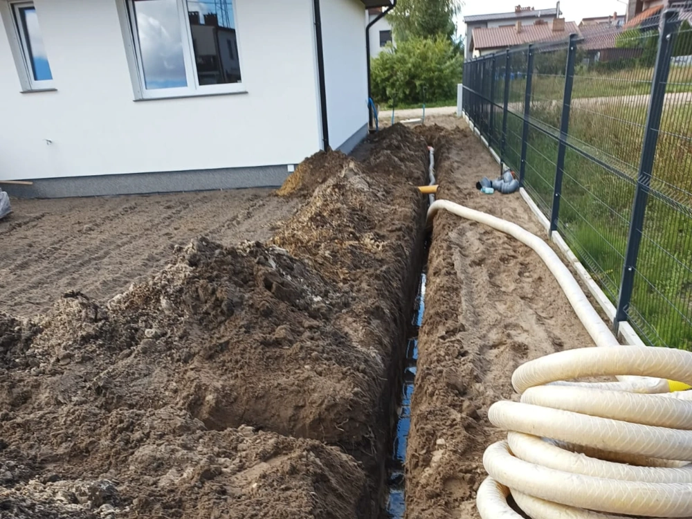 Wykopany rów drenażowy przy budynku z widoczną rurą drenarską do instalacji Drenaż