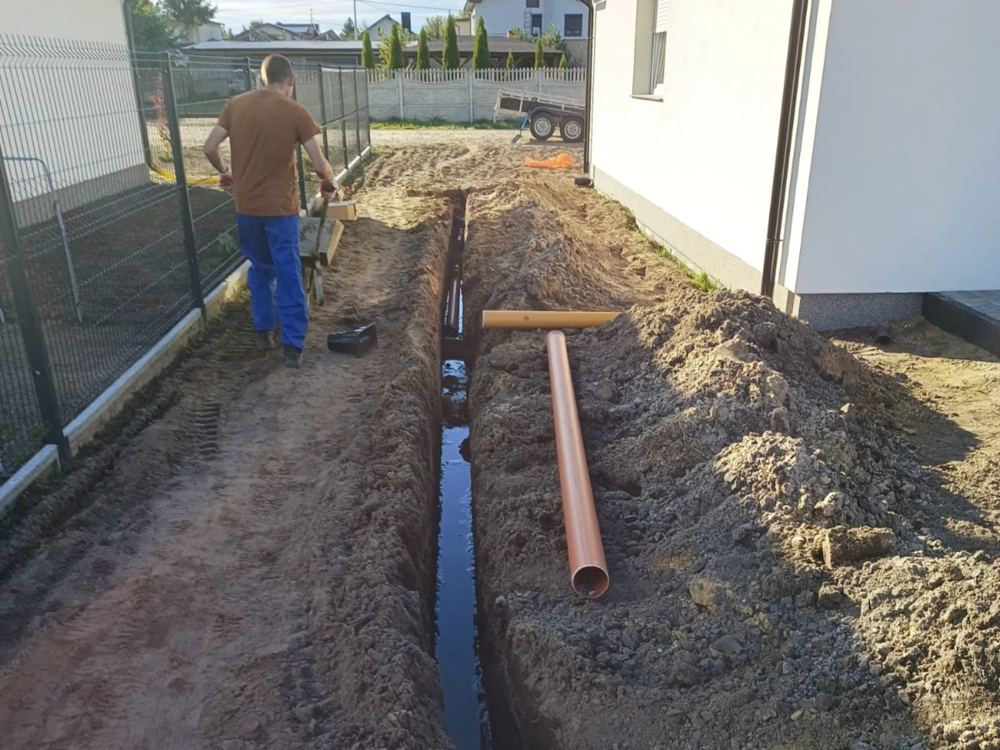 Układanie rur drenarskich w wykopie przy budynku Drenaż