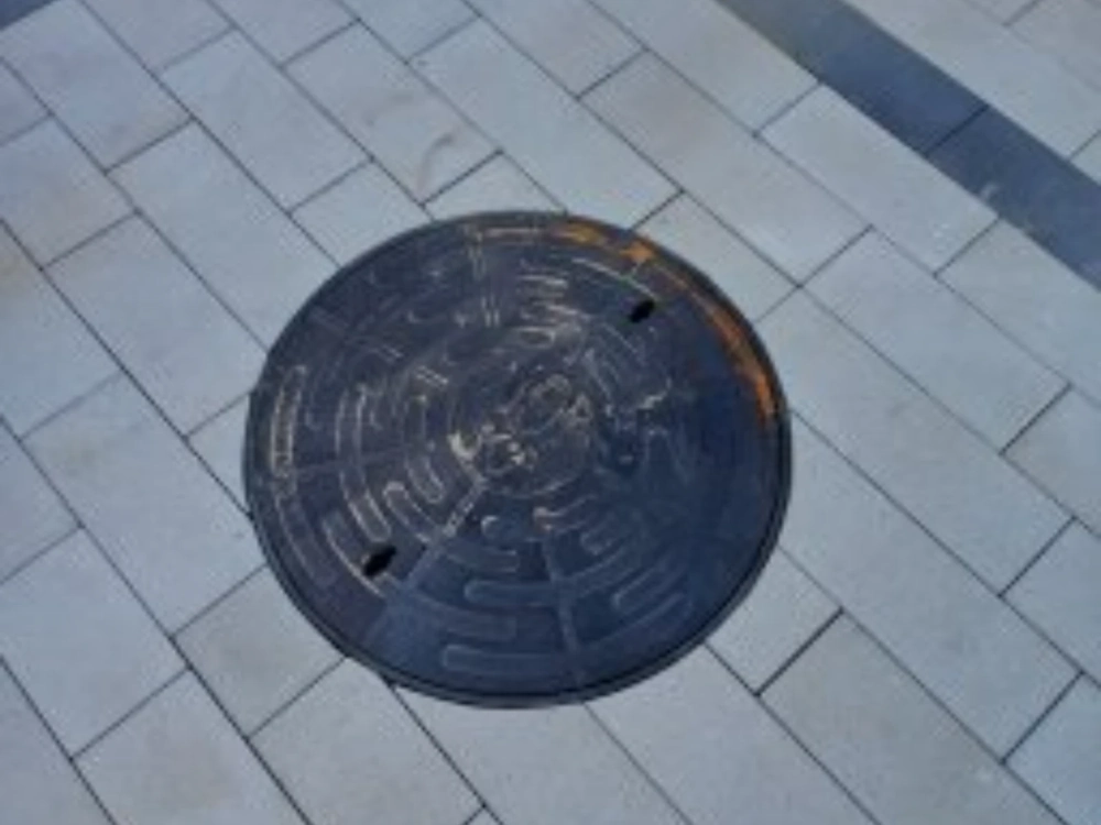 Układanie kostki brukowej wokół metalowego włazu kanalizacyjnego