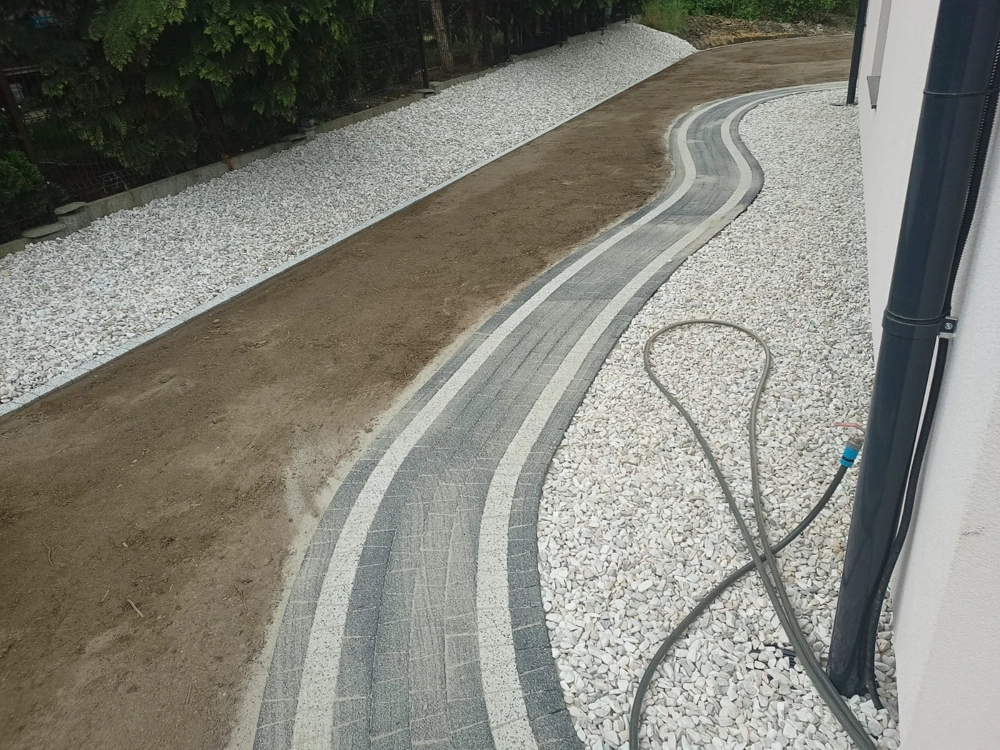 Opaska wokół domu z kostki brukowej z kontrastującymi pasami i obsypką z białego żwiru