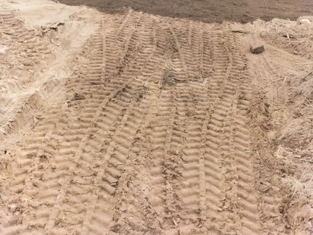 Niwelacja terenu z widocznymi śladami gąsienic maszyny na wyrównanym gruncie