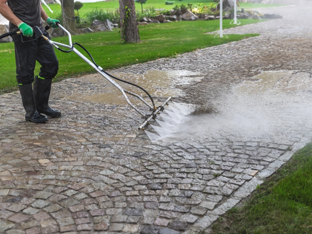 Czyszczenie kostki brukowej na podjeździe przy użyciu myjki ciśnieniowej w ogrodzie