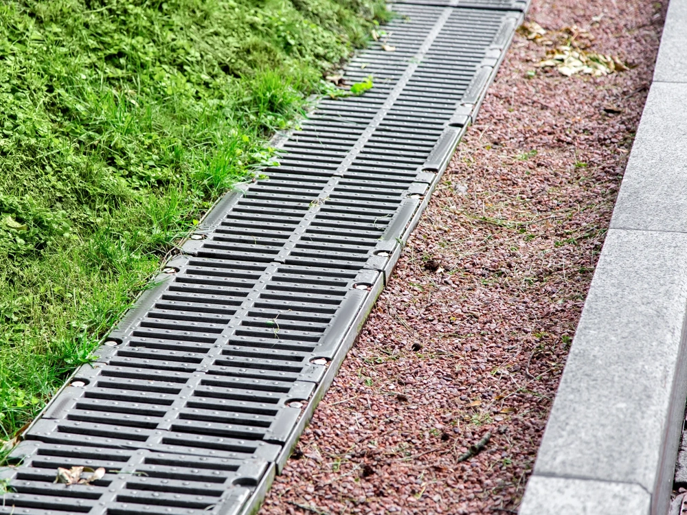 Odwodnienie liniowe z metalową kratą zamontowane przy trawniku i krawężniku