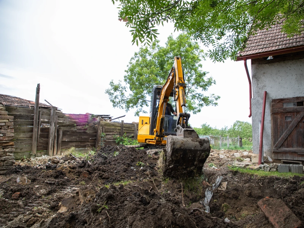 Usługi minikoparką – mała koparka wykonuje wykop ziemi przy budynku