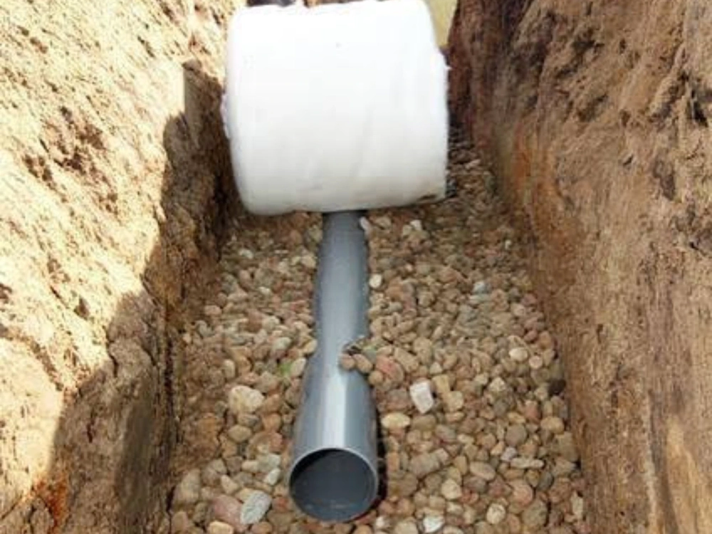 Montaż drenażu – rura drenarska ułożona w wykopie na warstwie żwiru